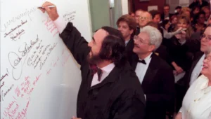 Luciano Pavarotti signs the wall as David DiChiera watches