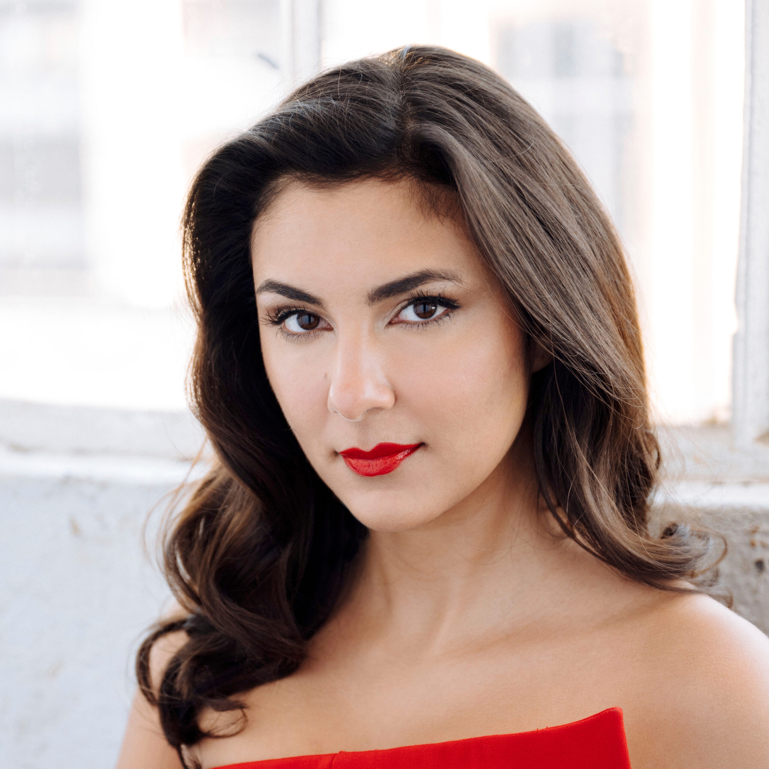 a photo of Cuban American soprano Elena Villalón sitting in front of a window. Villalón appears as Almirena in Handel's Rinaldo at Detroit Opera in February and March 2025